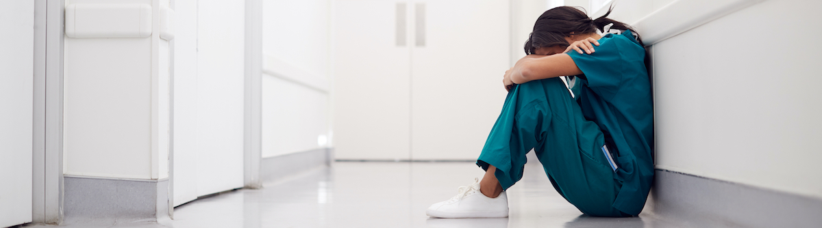 Stressed Nurse Sitting On Floor In Hospital Corridor